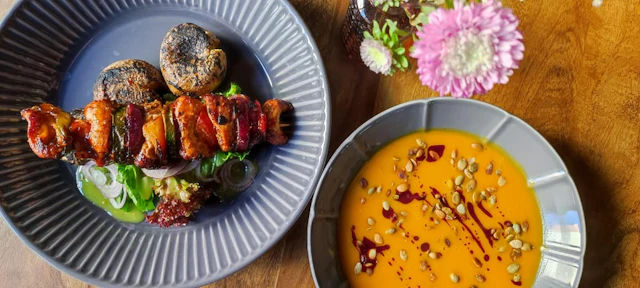 Szaszłyk i miska zupy sfotografowane na restauracyjnym stole.
